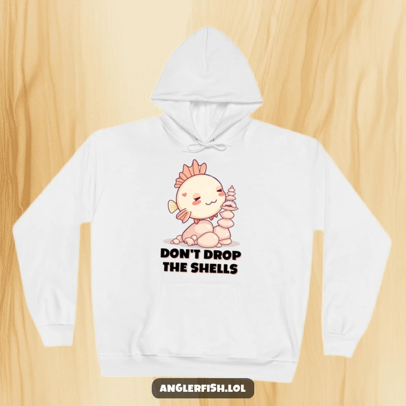 Funny Kawaii anglerfish hoodie showing a cute anglerfish struggling to keep seashells balanced in a comical pose.